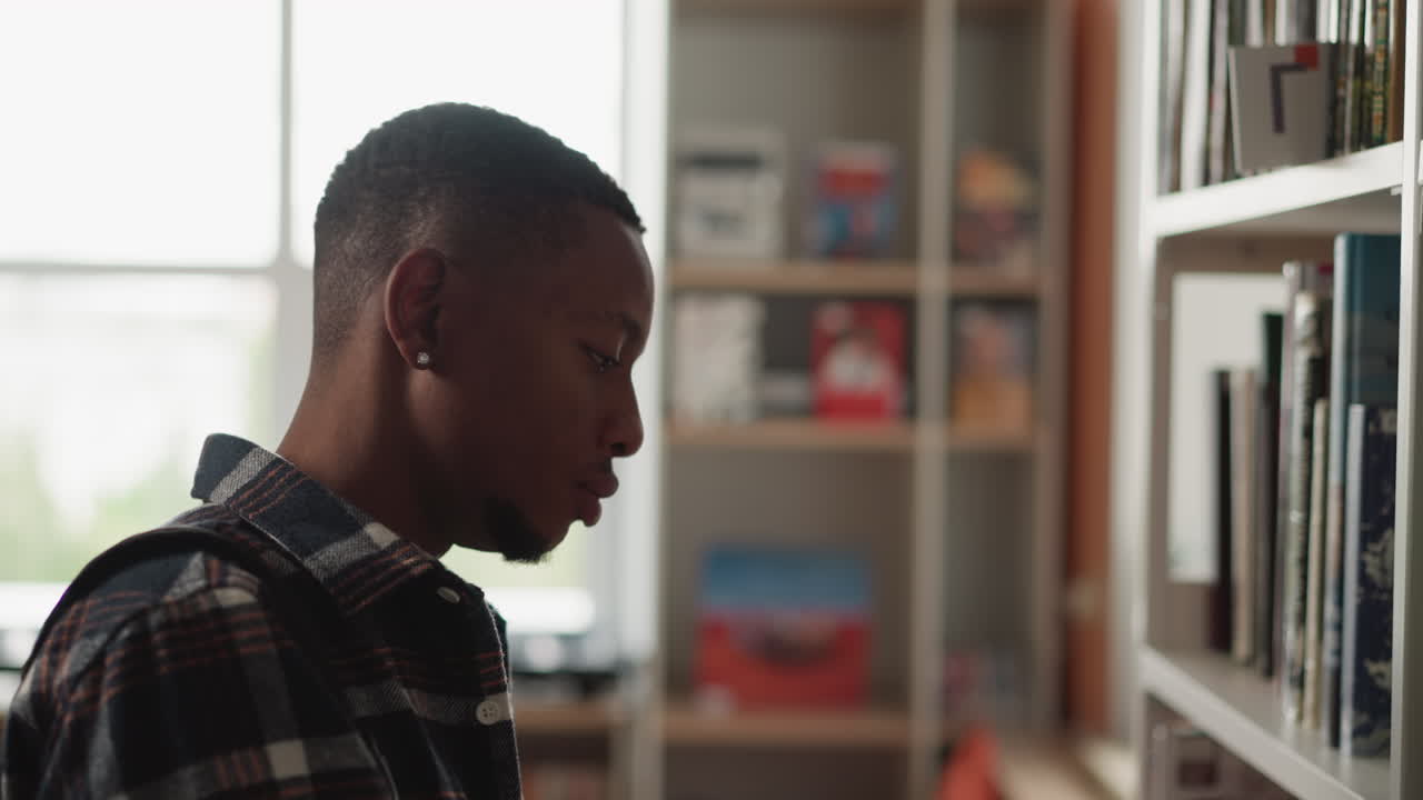 un hombre de piel oscura selecciona un libro en la tienda. un hombre afroamericano revisa el libro para obtener la información necesaria de pie en la librería. un estudiante busca el manual