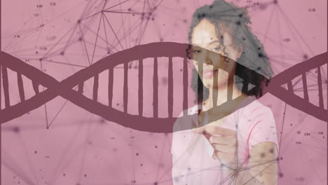 animation of dna strand and data processing over african american woman holding pink ribbon
