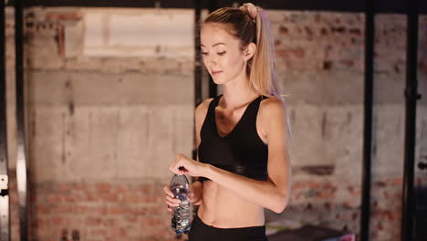 young female athlete drinking water from bottle after workout session at health club