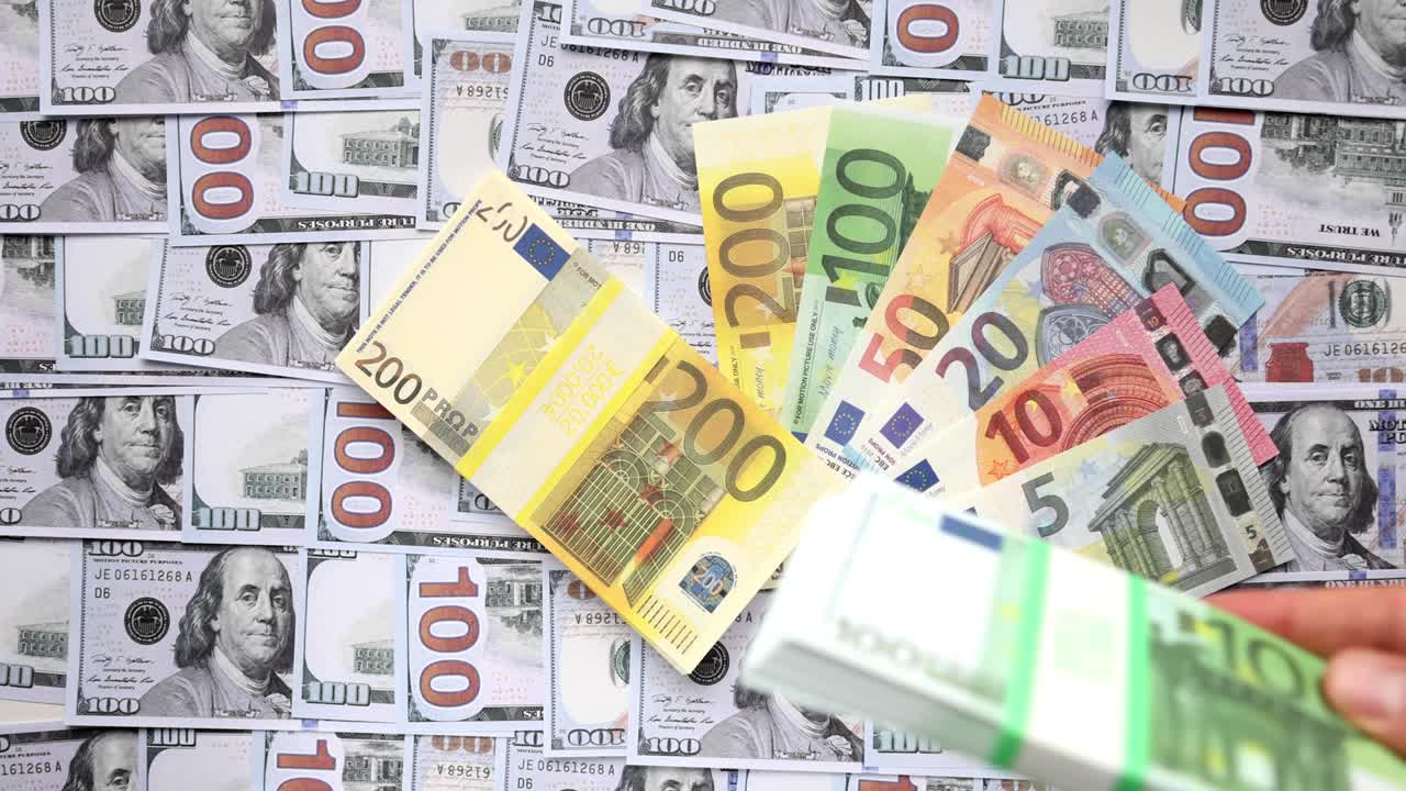 una persona que deja caer billetes de euros sobre un fondo con dólares estadounidenses.