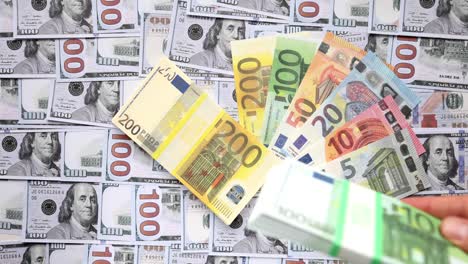 a person dropping euros banknotes on a background with american dollars.