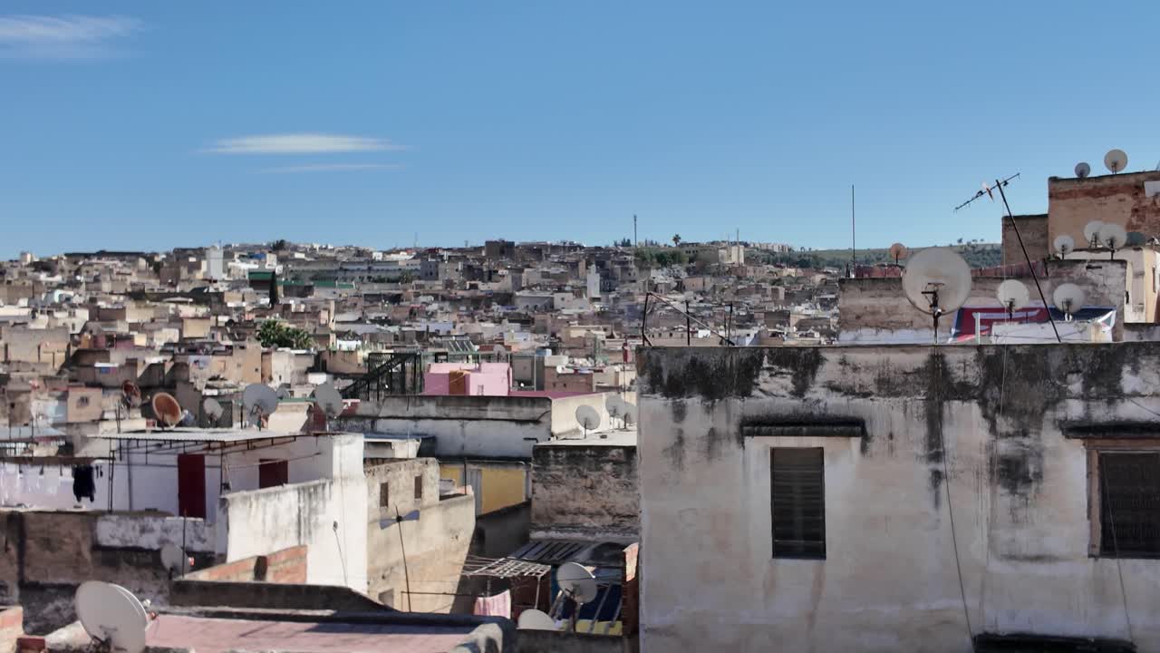 Cityscape of Fez featuring traditional buildings and vibrant rooftops under a clear blue sky, capturing the essence of Morocco's rich culture. Pan left