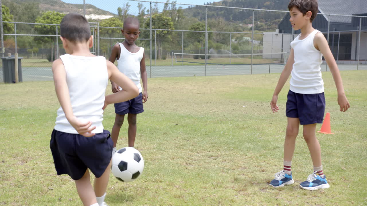 Na escola, três meninos jogando futebol no campo durante a aula de educação física.