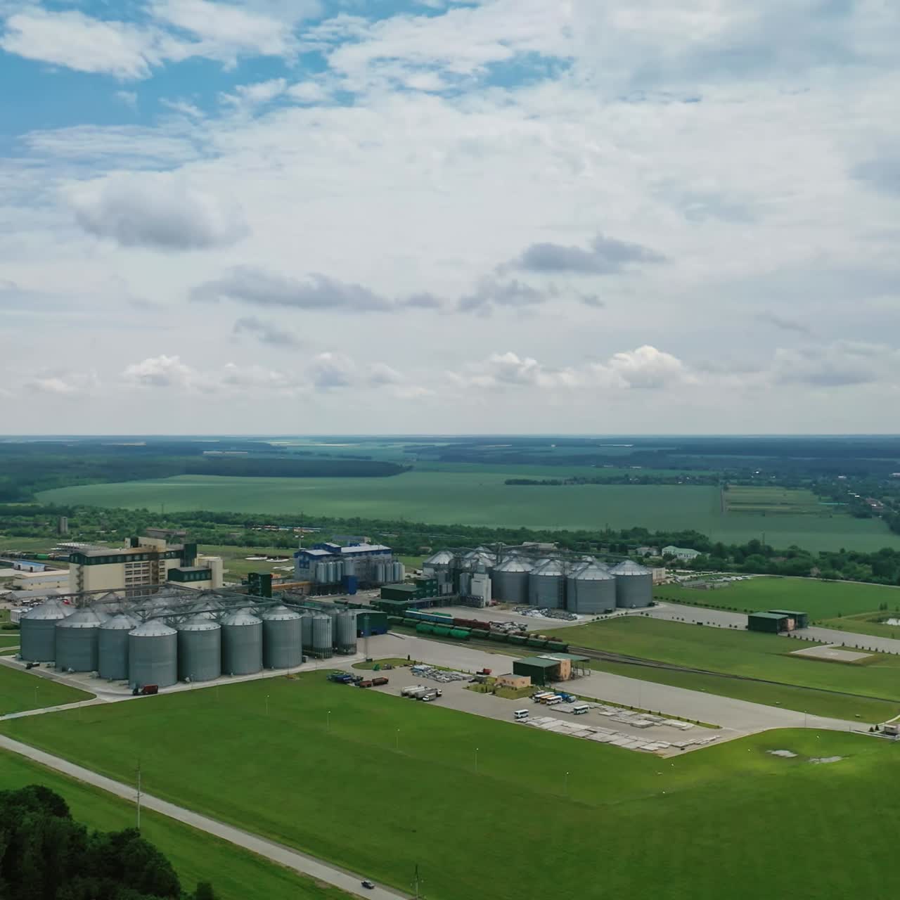 Agricultural area among green nature. Steel grain elevators on field. Plant for storage and processing of grain. Aerial view.