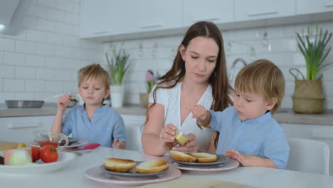 beautiful young mother with two children sons on white light kuna cook with burgers