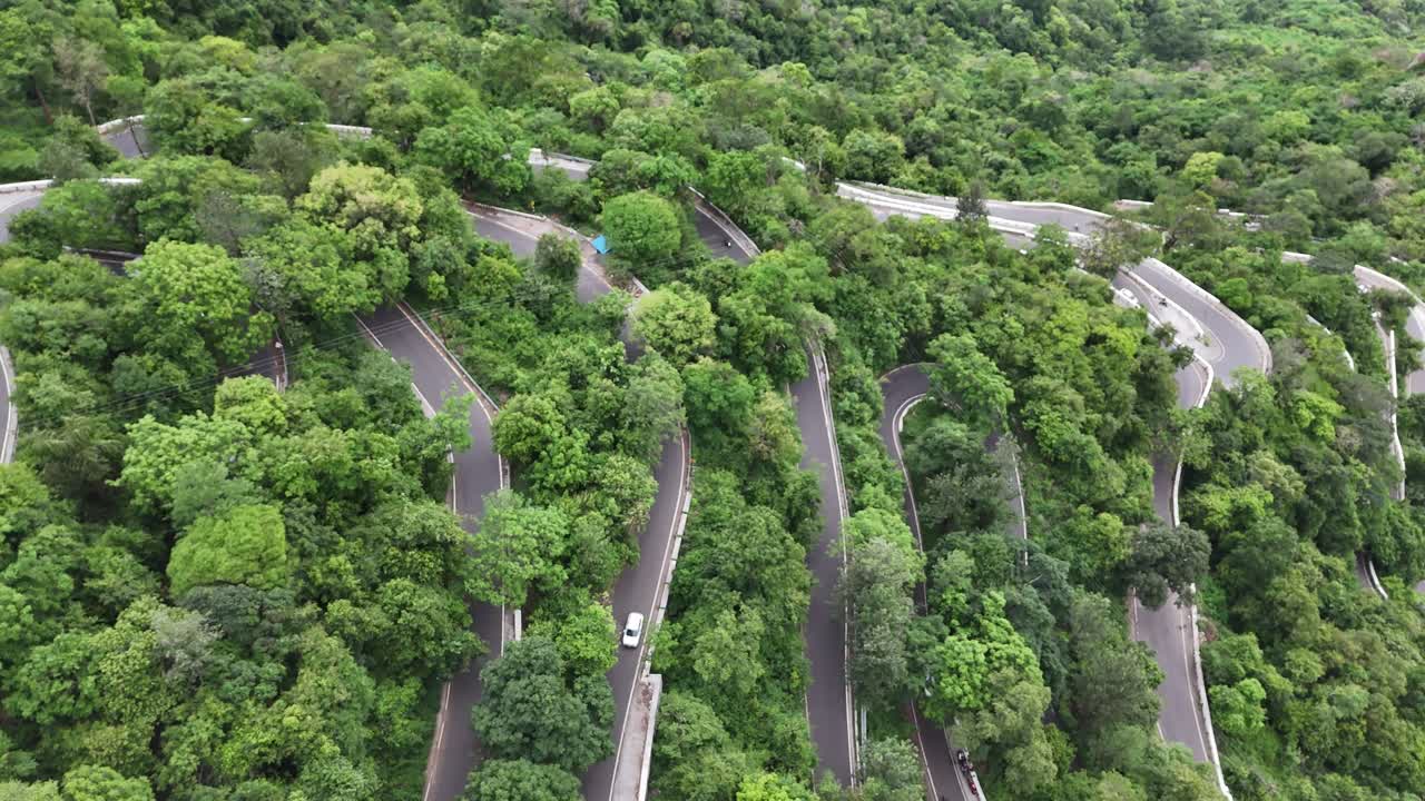 Drone shot of the serpentine ghat road at Kolli Hills, one of India's most challenging drives. The road is carved into the tropical, winding road is entirely surrounded by vibrant tropical forests