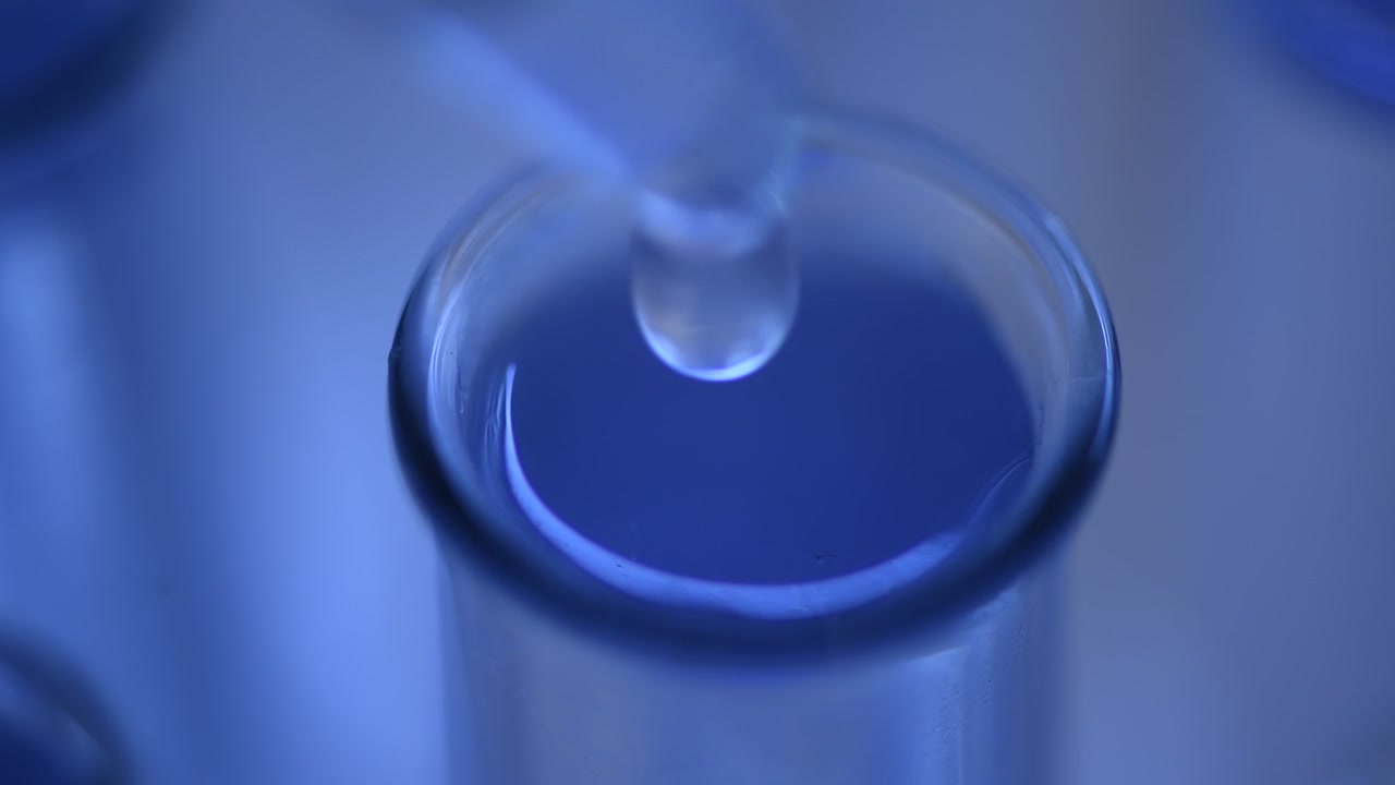 Primo piano di un contagocce che aggiunge liquido trasparente a una provetta blu
