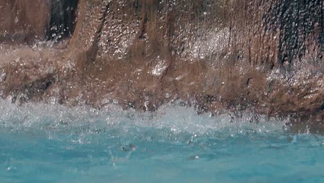 Gotas-De-Agua-Caen-Sobre-La-Superficie-De-La-Piscina-Contra-Las-Rocas-En-Cámara-Lenta