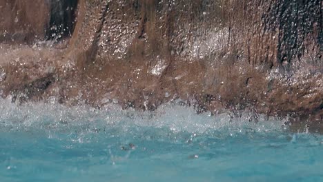 gotas de agua caen en la superficie de la piscina contra las rocas en cámara lenta
