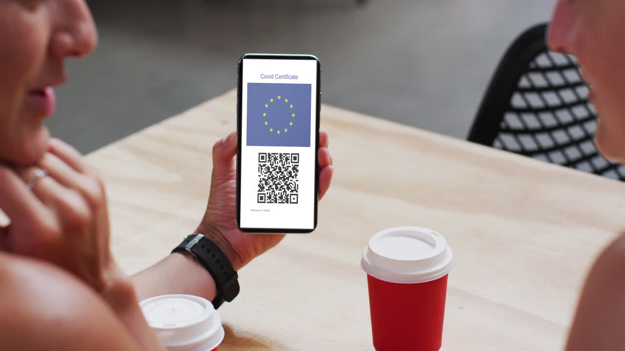 Man at cafe showing smartphone with covid vaccination certificate, eu flag and qr code on screen