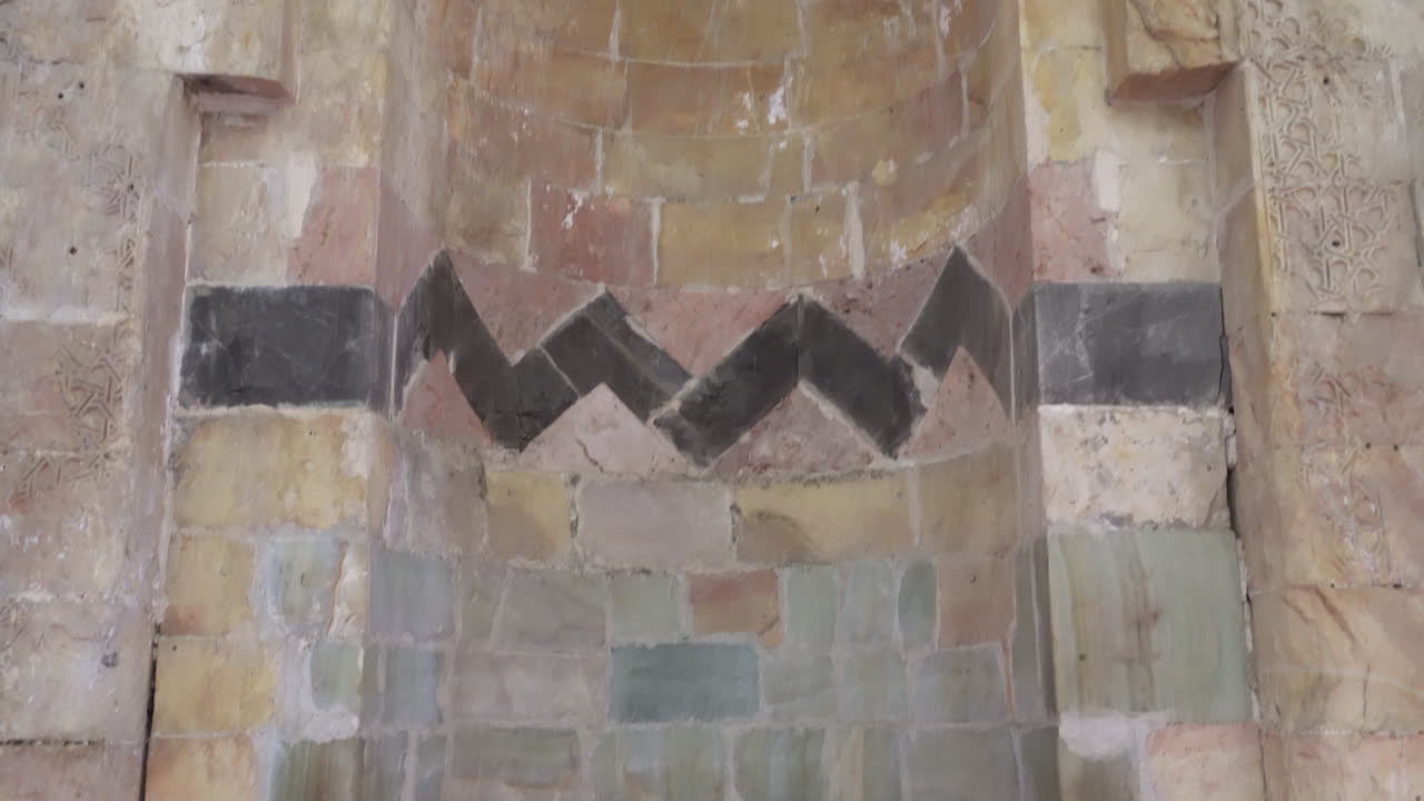 카메라는 징키리예 마드라사의 다듬은 돌 미흐랍을 아래에서 위로 스캔하고 마침내 우리는 미흐랍에 새겨진 돌 비문을 봅니다.