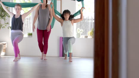 diverse fitness teenage girls in aerial yoga class with female coach in big white room, slow motion