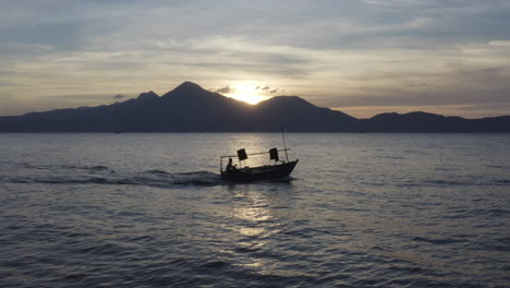 fishing boat motors out to ocean at sunset against a beautiful landscape in asia