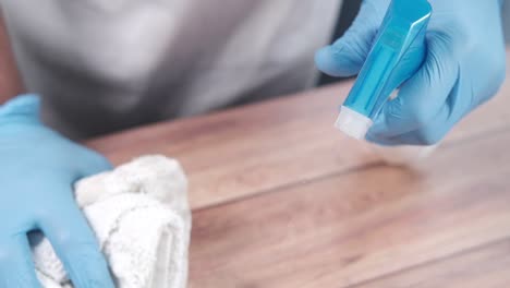 cleaning a wooden table with spray bottle and gloves