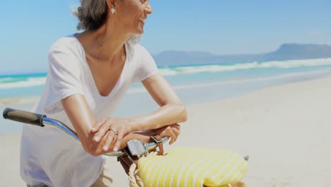 Front-view-of-active-senior-African-American-woman-leaning-on-bicycle-handlebars-on-the-beach-4k