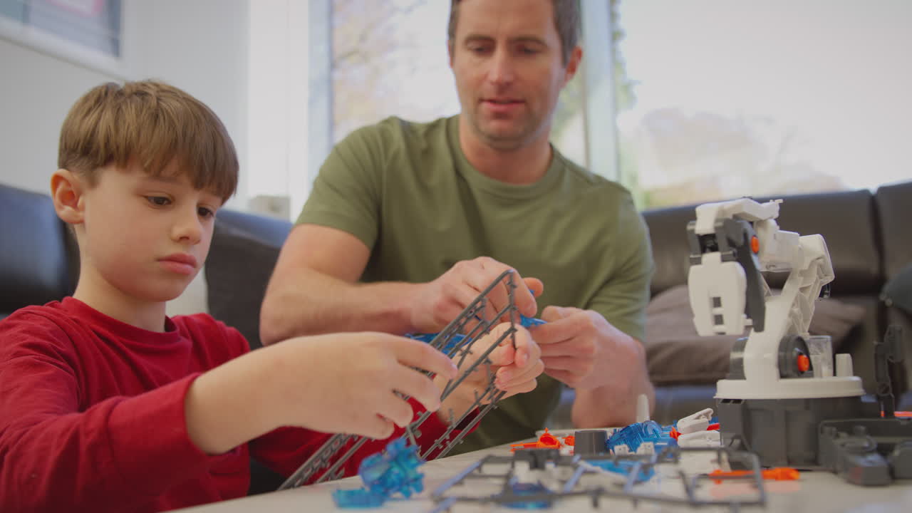 padre e hijo con pijama construyendo un brazo robótico a partir de un kit de plástico en casa para un proyecto científico - filmado en cámara lenta