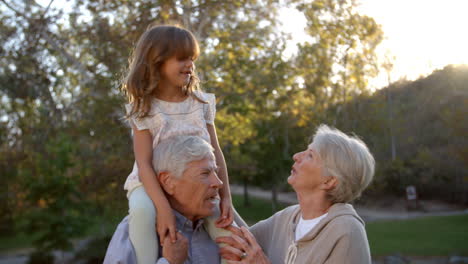 grandparents giving granddaughter a shoulder ride in park