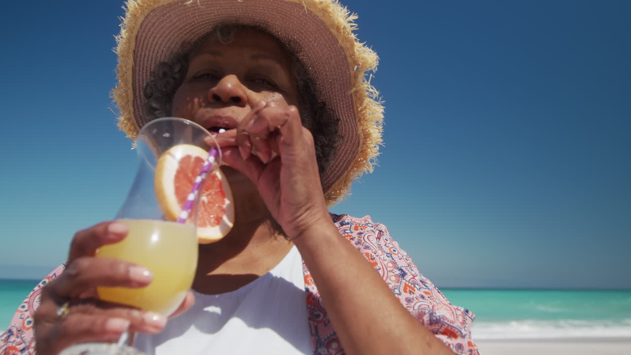 una mujer mayor bebiendo un cóctel en la playa.