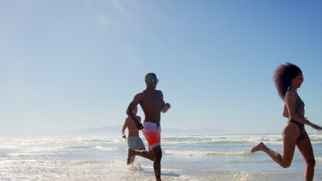 Grupo-De-Amigos-Corriendo-Entre-Olas-En-Vacaciones-En-La-Playa