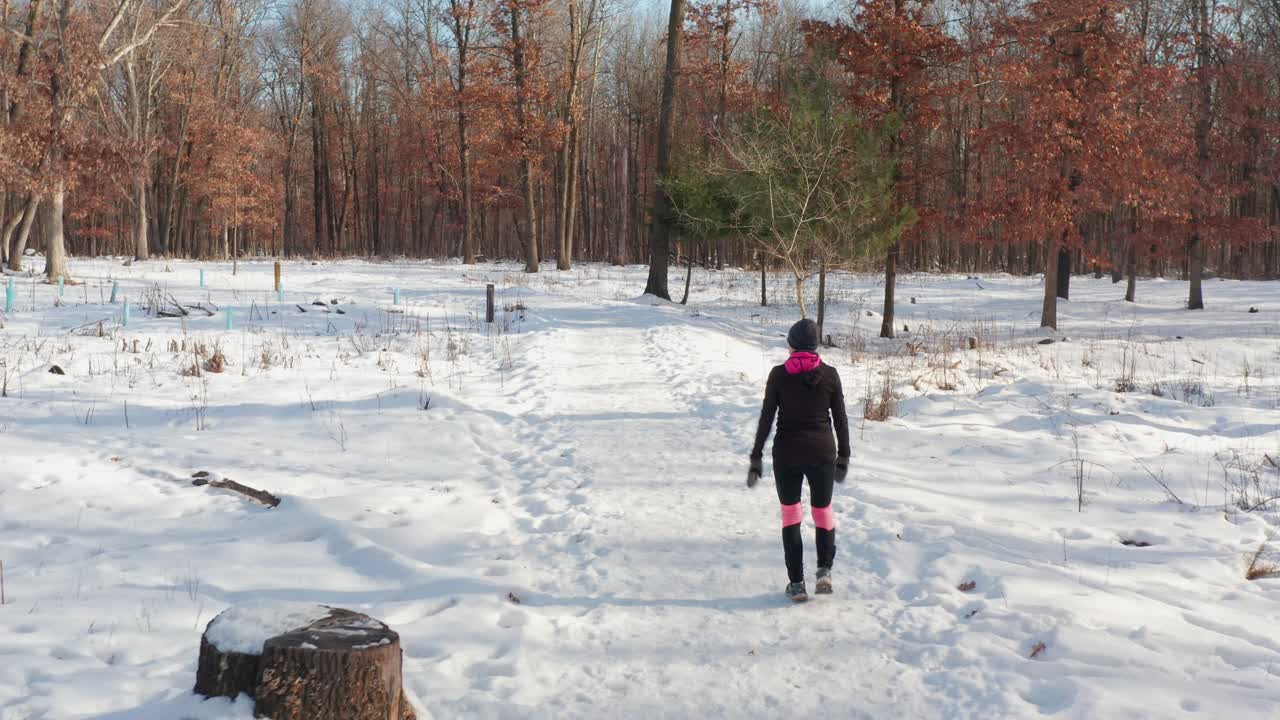 Woman walking alone on snowy winter forest path
