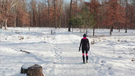 Woman-walking-alone-on-snowy-winter-forest-path