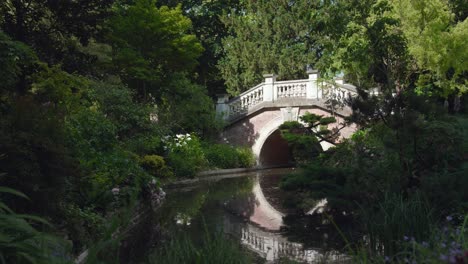 static view of parc monceau with beautiful stone bride across river on summer day in paris, france