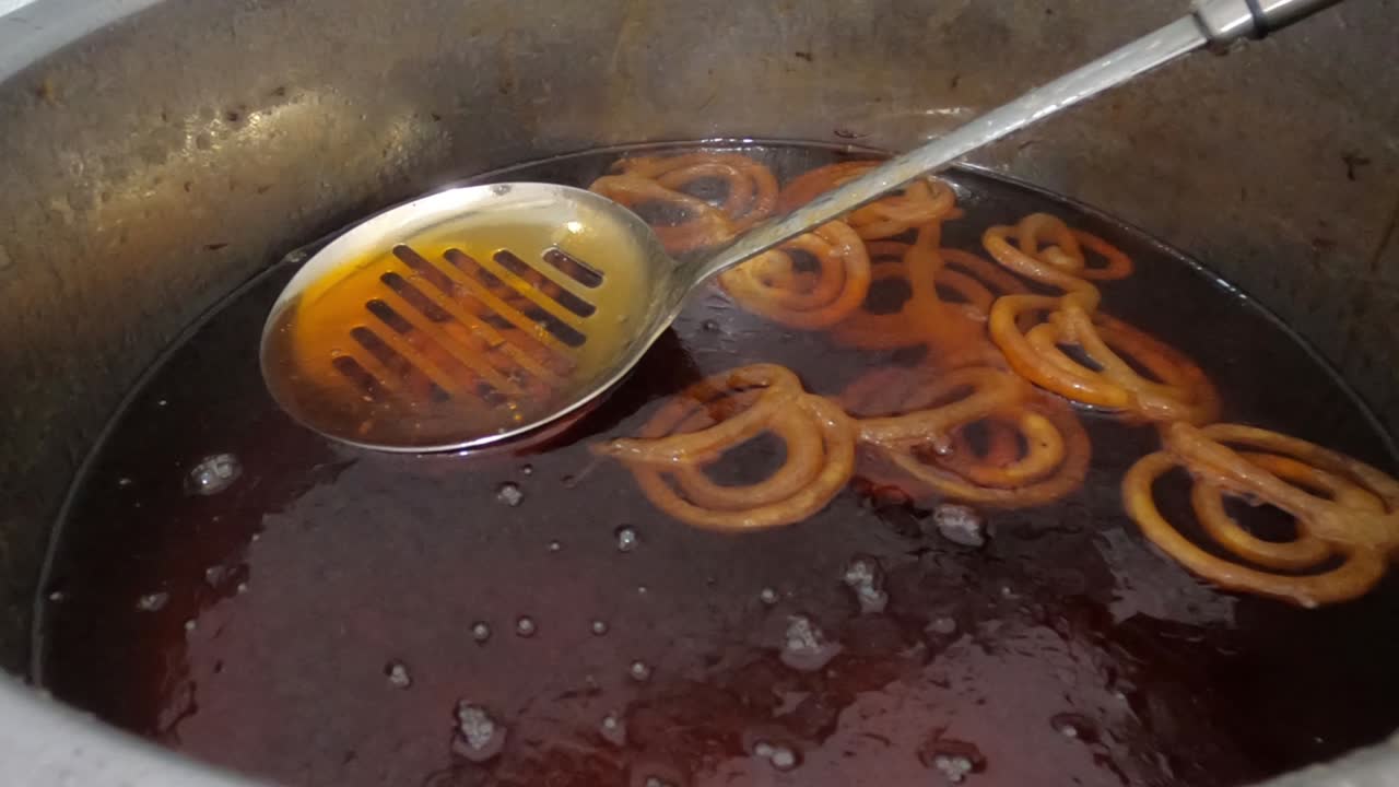 Raw jilapi deep frying 4k video clip.Jilapi making on a hot big pan.Jalebi, also known as jilapi, jilebi, jilipi, zulbia, jerry, mushabak, or zalabia, is a popular Indian sweet snack.