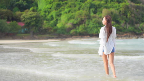 예쁜 젊은 여자가 들어오는 파도 속에서 혼자 걷는다