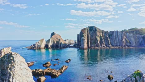 drone flying through vertical coastal rocks jutting into sea in idyllic summer setting