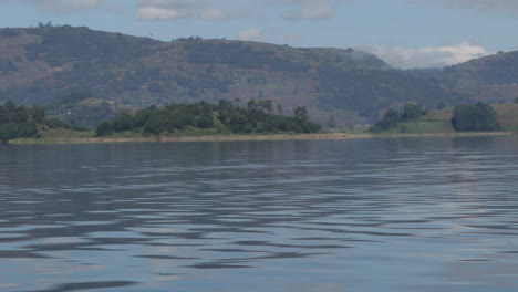 Riding-a-boat-on-a-peaceful-lake-with-mountains-in-the-background-in-Kampala,-Uganda