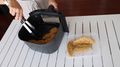 a person uses tongs to transfer cooked chicken from an air fryer to a tray on a white table