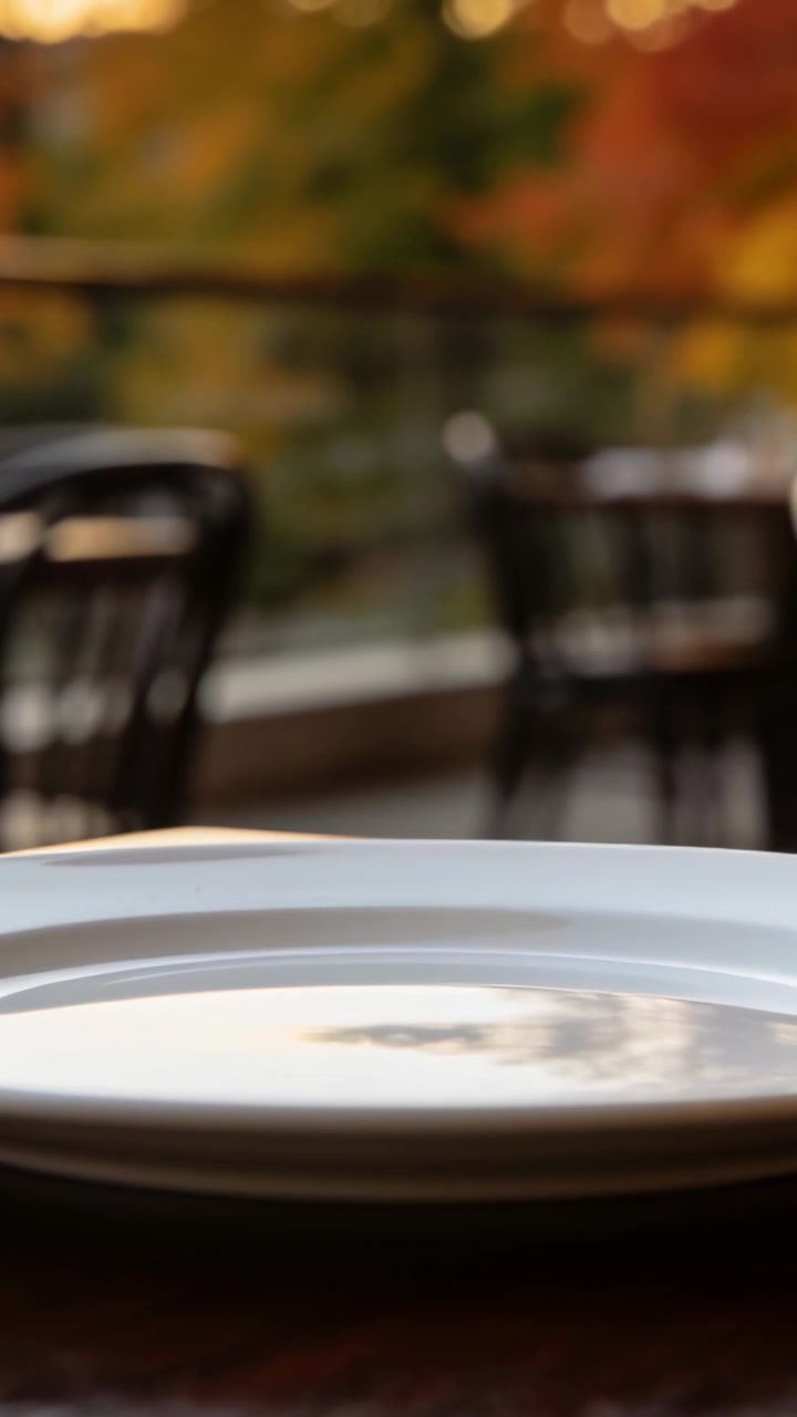 Video verticale: La telecamera sposta delicatamente il fuoco su un tavolo da patio, mostrando piatti bianchi impilati e un bokeh caldo
