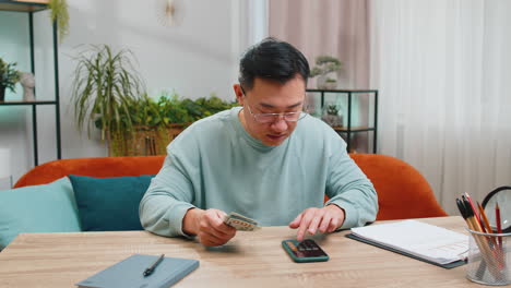 rich happy asian man counting money cash on smartphone calculator app, calculate income earnings