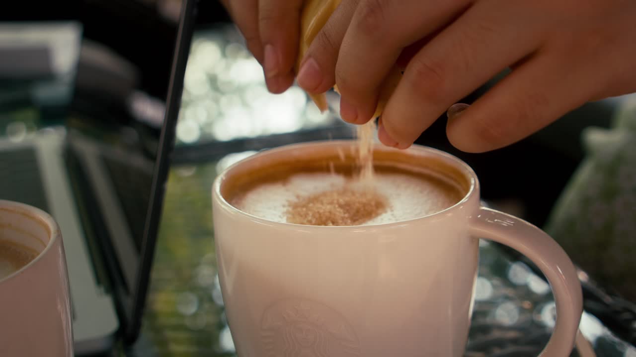 Primo piano con messa a fuoco selettiva mentre si versa lo zucchero in un caffè latte.