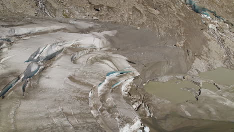 Aerial-closeup-of-debris-covered-Pasterze-glacier-melting-ice-pond,-Retreating-glacier-muddy-water-pond