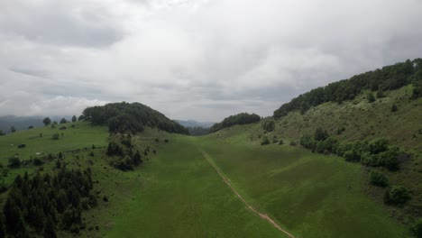 Lush-green-hills-under-a-cloudy-sky,-aerial-view-of-a-serene-landscape