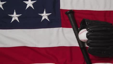 overhead baseball still life with bat and catchers mitt on american flag with ball rolling into frame 1