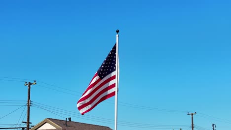 American-Flag-drone-view-flying-around-with-view-of-power-lines,-roofs,-and-blue-sky-with-no-clouds