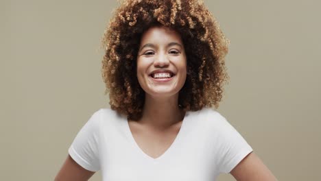 Happy-biracial-woman-with-dark-curly-hair-with-copy-space-on-beige-background,-slow-motion