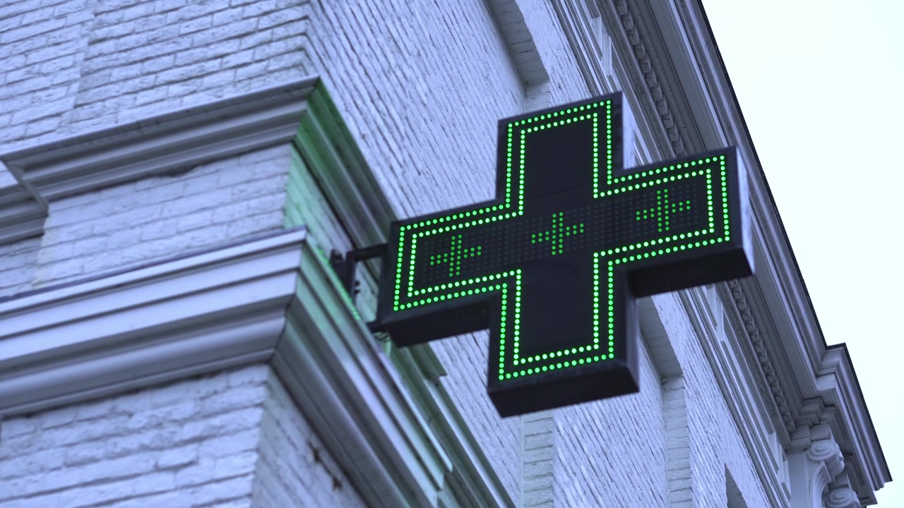 Insegna a croce verde di farmacia appesa al muro vicino alla farmacia, illuminata e lampeggiante per le strade. Periodo invernale.