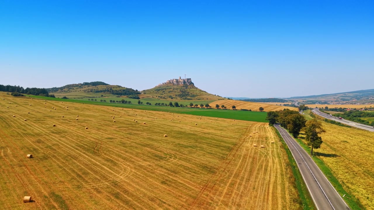 Colline ondulate e balle di fieno in un campo. Balle di fieno si trovano in un campo vicino a una collina con un castello. Questa scena mostra cieli sereni e paesaggi verdi in campagna.
