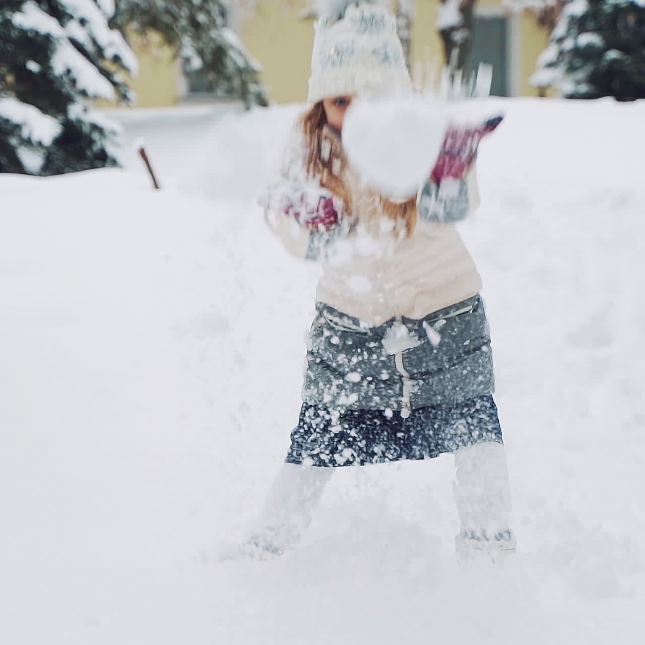 Beautiful smiling girl throwing white snow up and looking at camera in winter. Little child is playing in snow outside. Fun with snow. Slow motion.