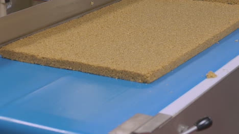 a worker flips a slab of flapjack cake onto a conveyor belt