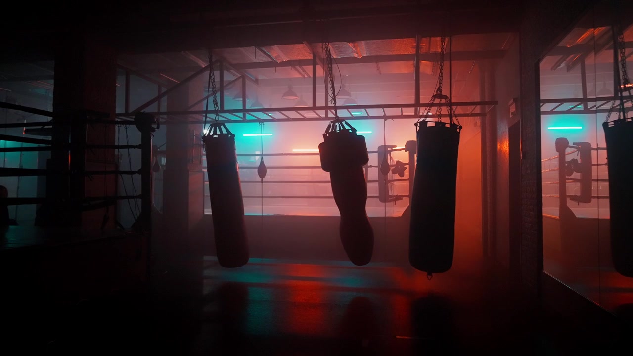 Suggestiva palestra di pugilato vuota con sacchi da boxe e luci al neon
