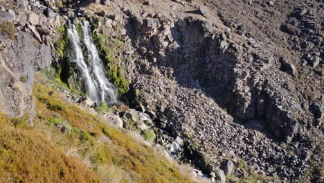 pequeña cascada alpina divide la pendiente de hierba de matas de roca estéril