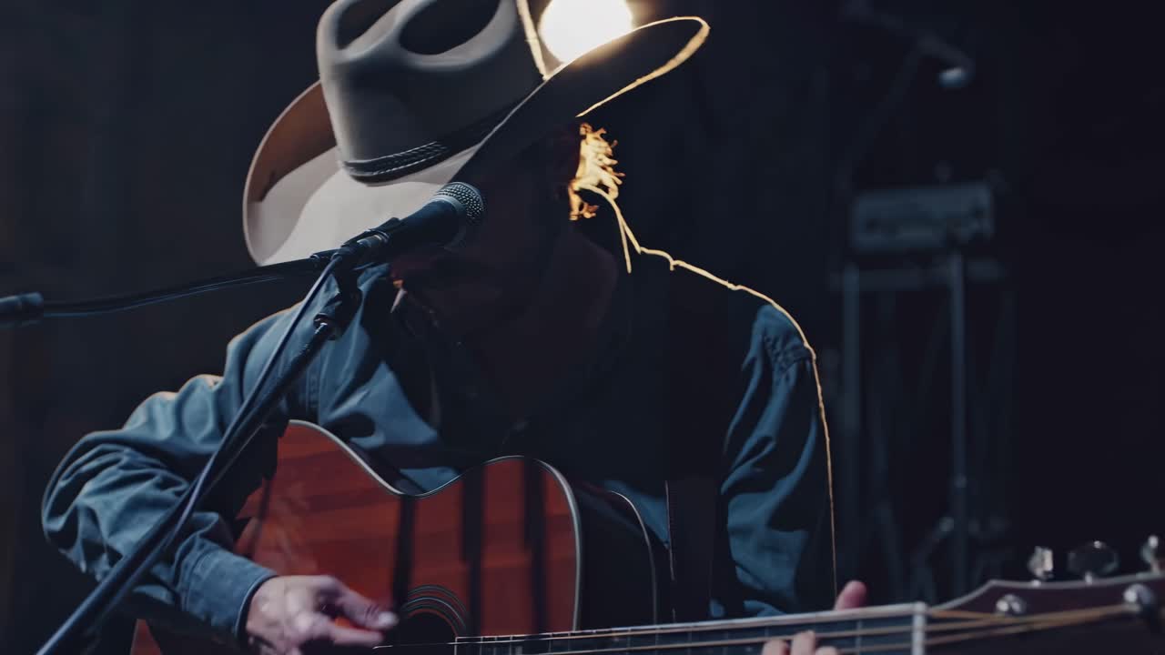 Low-angle video shot of a musician in a cowboy hat playing guitar under warm stage lights