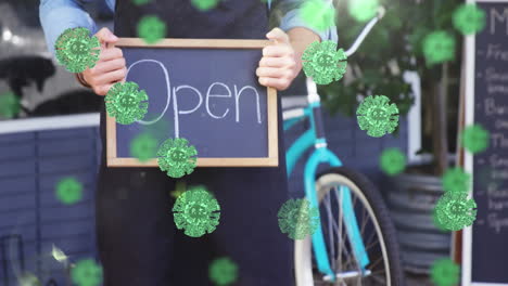 animation of macro covid-19 cells floating over happy caucasian male chef holding open sign