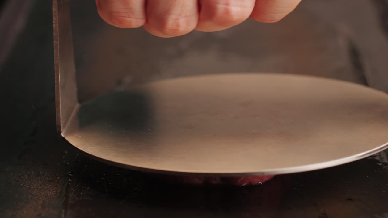 Cooking American fat smash burger on grill close-up. Beef or pork cutlet smashing by burger press. The chef in kitchen of the restaurant making cutlets for burgers - smash burger beefsteak. Fast and street food concept. High quality 4k footage