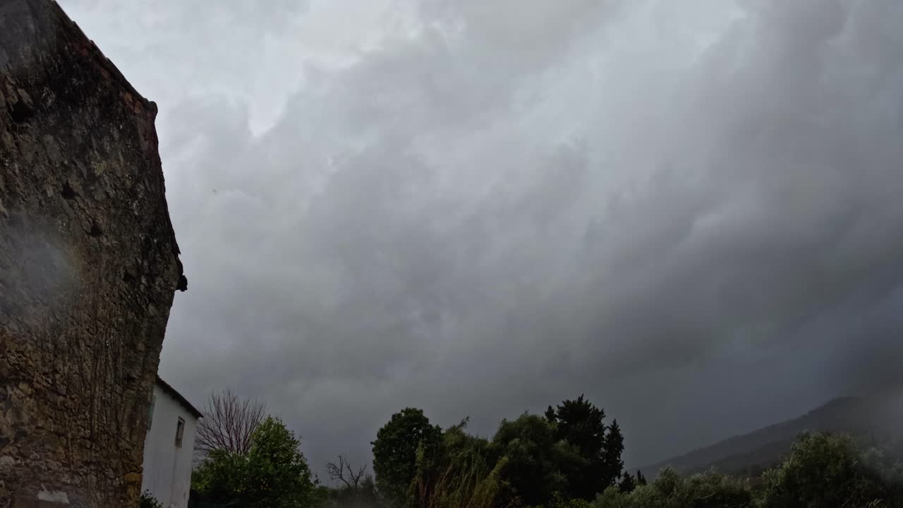 Time lapse de nubes de tormenta oscuras y espectaculares que se mueven rápidamente sobre una antigua casa de piedra y un paisaje rural verde en Corfú (Grecia) antes de una lluvia intensa