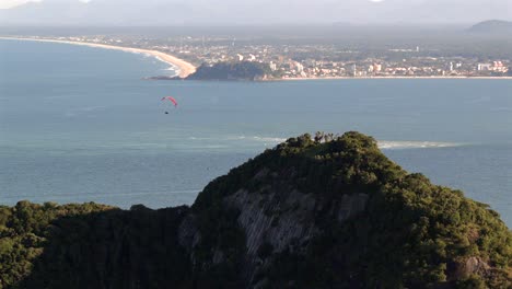 Distant Caiobá beach with Matinhos and Guaratuba municipality skyline with hills and flying parachute from above, Paraná, Brazil
